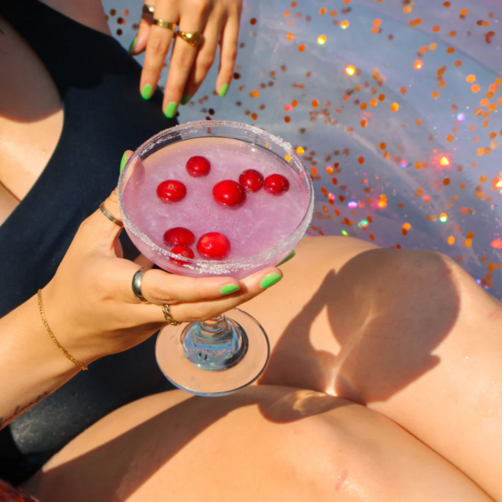 A Summer Cocktail Bomb Variety Pack, featuring colorful, fruit-flavored drink mixers in a white box, with a hand picking up a yellow cocktail bomb. The image includes strawberries, pineapples, and limes against a bright blue background. Available in Ottawa, Ontario, Canada.