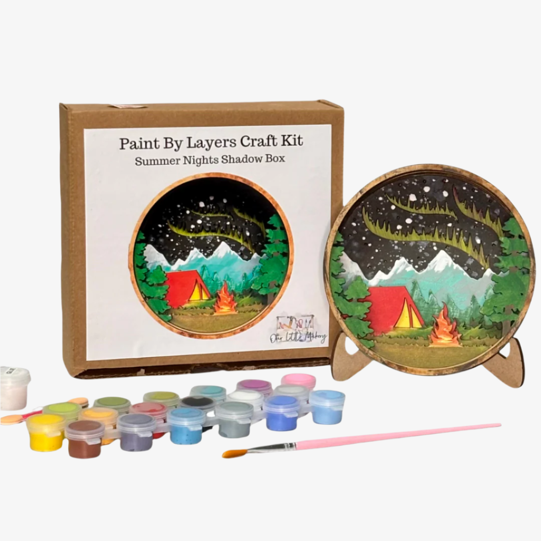 Paint by layers craft kit with a completed painting of a tent and campfire, surrounded by paint containers and a brush.