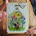 Card with a bottle of flowers and a character, held by a person.