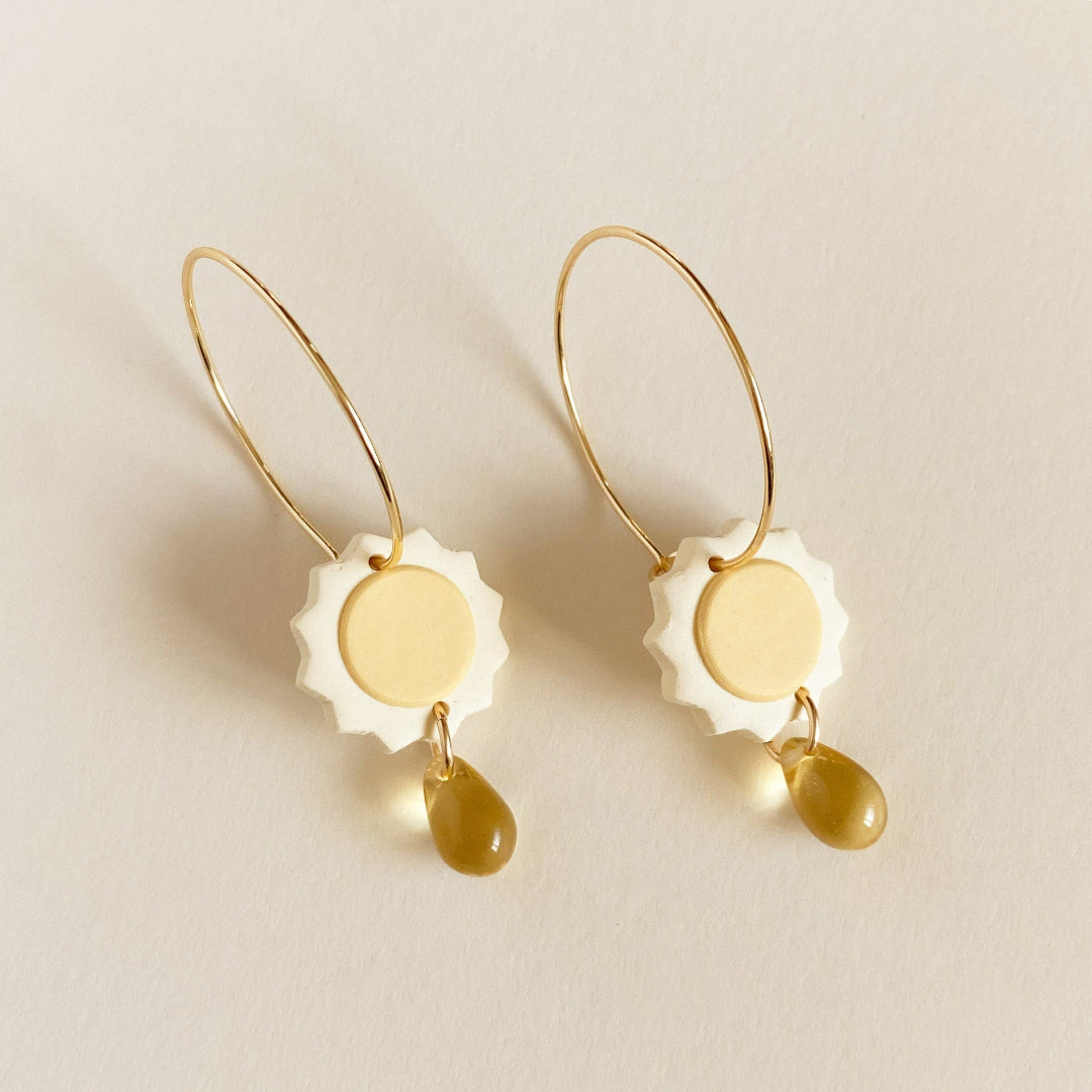 Pair of earrings with gold and white design on a beige background