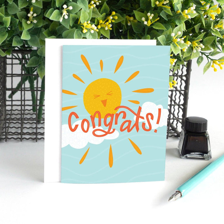 A congratulations card featuring a smiling sun with rays shining on clouds. The text 