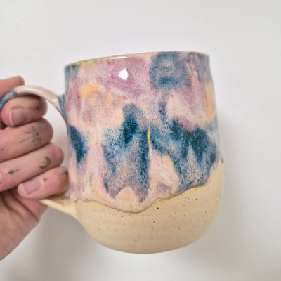 Hand holding a ceramic mug with multicolored abstract design on a plain background
