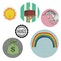 A clear plastic package containing six colorful pin-back buttons. The header card of the package reads "The Regional Assembly of Text PACK OF BUTTONS" and features a yellow shield with "IT'S ALL SUNSHINE AND RAINBOWS" inside, and "TO WEAR AND SHARE" below. Visible buttons include a unicorn, a sun, and a design with stripes and a building.