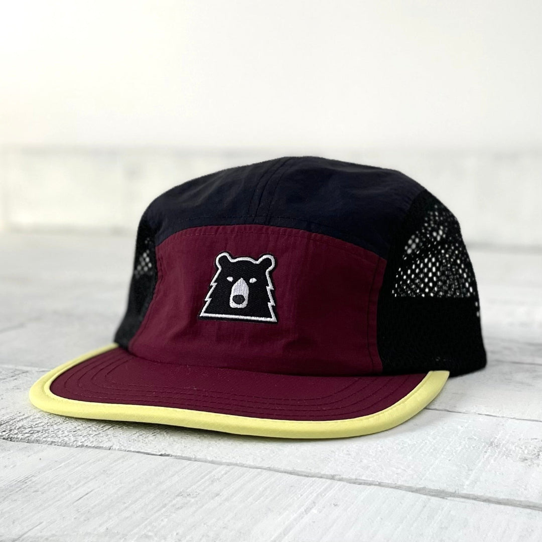Black and maroon cap with a bear logo on a light wooden surface