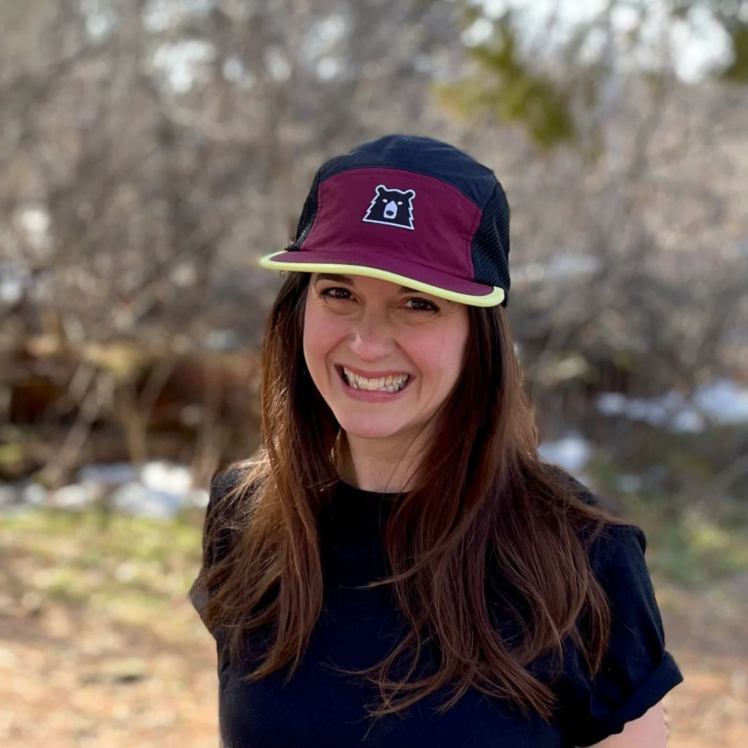 Person wearing a maroon and navy cap with a bear logo outdoors