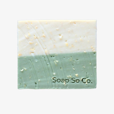 Two-tone soap bar with visible texture on a black background, branded 'Soap So Co'.