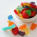 Assorted colorful gummy candies on a white surface with a bowl of more candies.