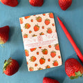 Notebook with strawberry pattern surrounded by strawberries on a blue background