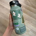 Green water bottle with nature-themed design held by a hand on a wooden surface