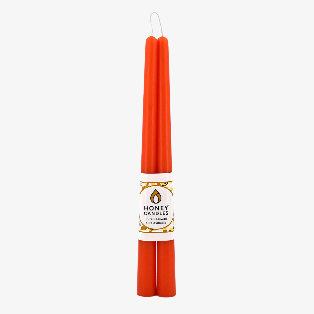Two orange beeswax candles are standing upright, tied together with a string. The candles have a label that says "HONEY CANDLES Pure Beeswax."