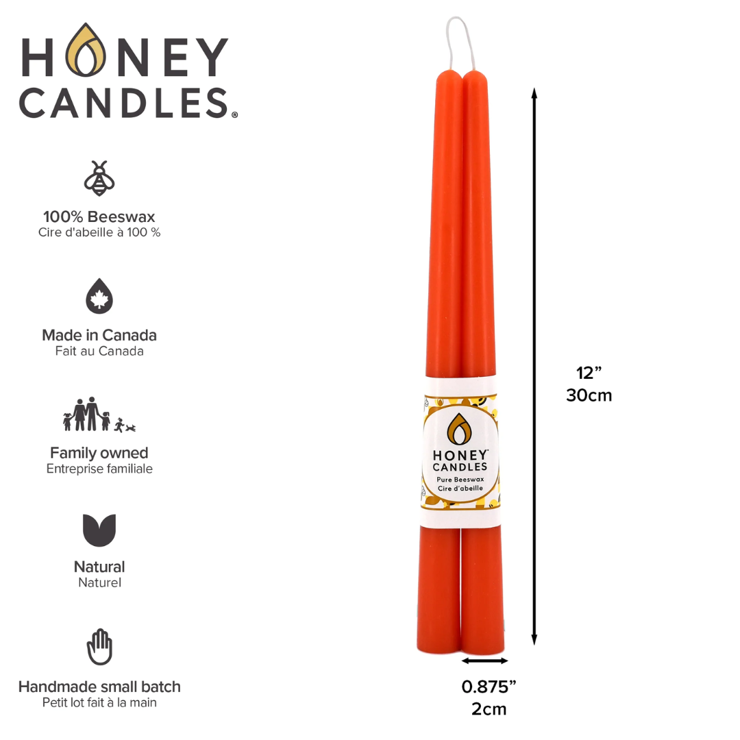 Two orange beeswax candles are standing upright on a white background. They are tied together with a string and have a label that says "HONEY CANDLES 100% Pure Beeswax" and a honeycomb pattern. The label also includes information about the candles, such as the fact that they are made in Canada, family-owned, and handmade in small batches.