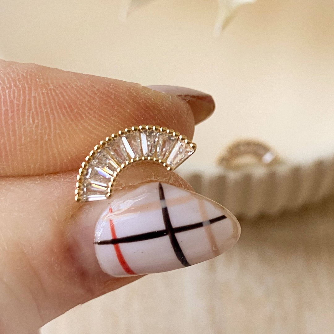 A pair of gold-plated stud earrings with a semicircle design. The earrings are adorned with multiple small cubic zirconia stones arranged in a fan shape.