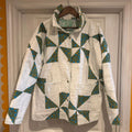 A vintage quilted jacket with a geometric triangle pattern in teal, blue, and yellow on an off-white background, hanging on a wooden hanger against a white paneled door.