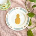 Decorative plate with a gold pineapple design on a textured surface with leaves.