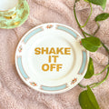 Decorative plate with 'SHAKE IT OFF' text on a textured surface with leaves.