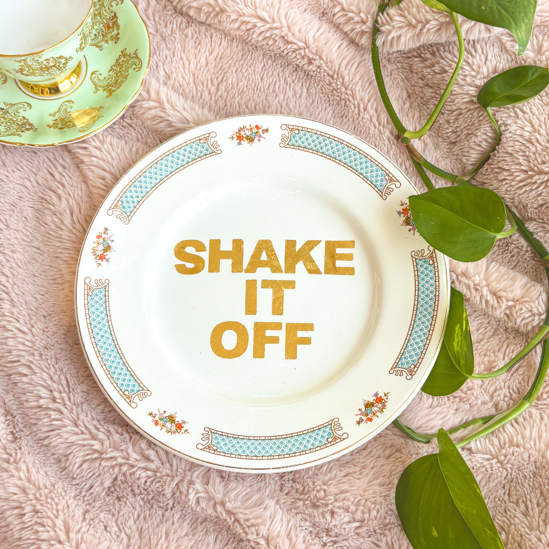 Decorative plate with 'SHAKE IT OFF' text on a textured surface with leaves.