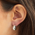 Close-up of an ear wearing a silver teardrop earring with blurred background