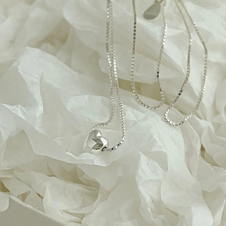 A teeny tiny heart necklace made of polished silver, featuring a very small, solid heart pendant on a delicate chain, displayed on a white background. This minimalist necklace is available in Ottawa, Ontario, Canada.