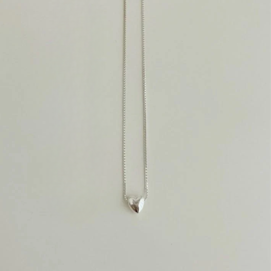 A teeny tiny heart necklace made of polished silver, featuring a very small, solid heart pendant on a delicate chain, displayed on a white background. This minimalist necklace is available in Ottawa, Ontario, Canada.