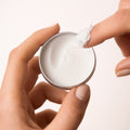 A small, open, silver metal tin of Everist's "The Fragrance-Free Body Wash Concentrate Travel Mini," revealing a white solid product inside. The tin's lid is propped against the base, and text on the side indicates it's dermatologist-developed and contains 20ml of product.