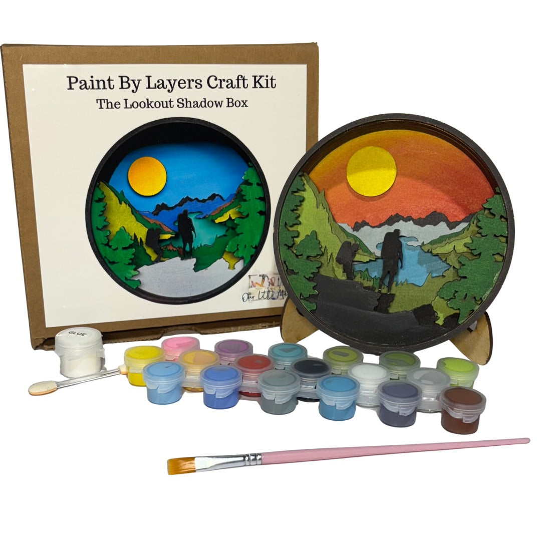 Paint by layers craft kit with scenic design, paint cans, and brushes on a white background