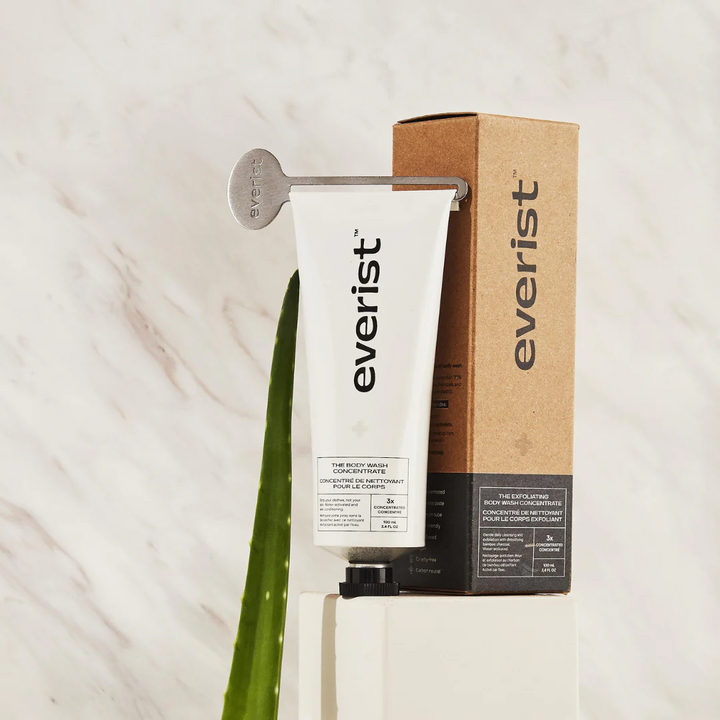 The Exfoliating Body Wash Concentrate tube on a pedestal with the key and the box. This waterless body scrub is perfect for any skin type.