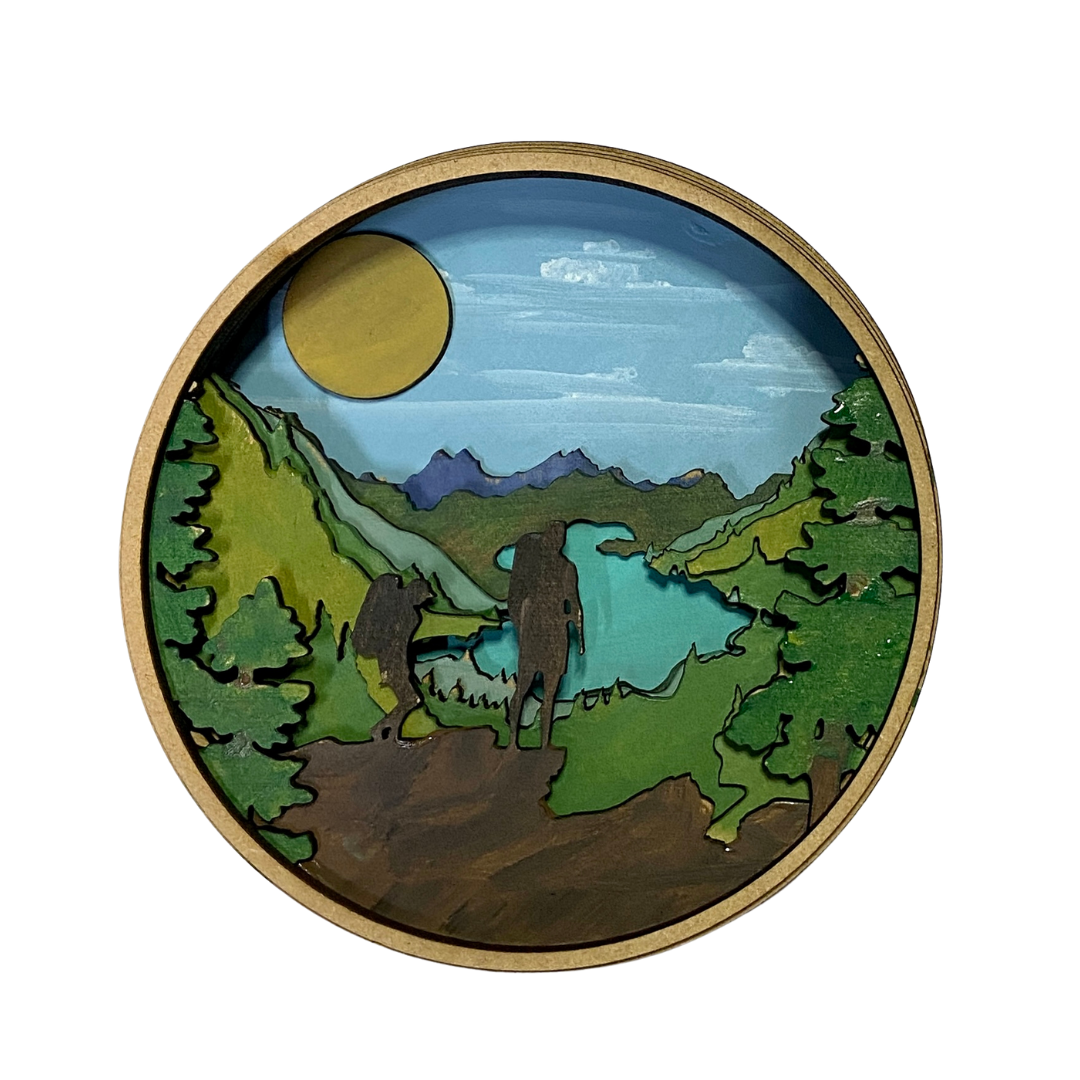 Round wooden plaque with a landscape design featuring trees, mountains, and a lake.