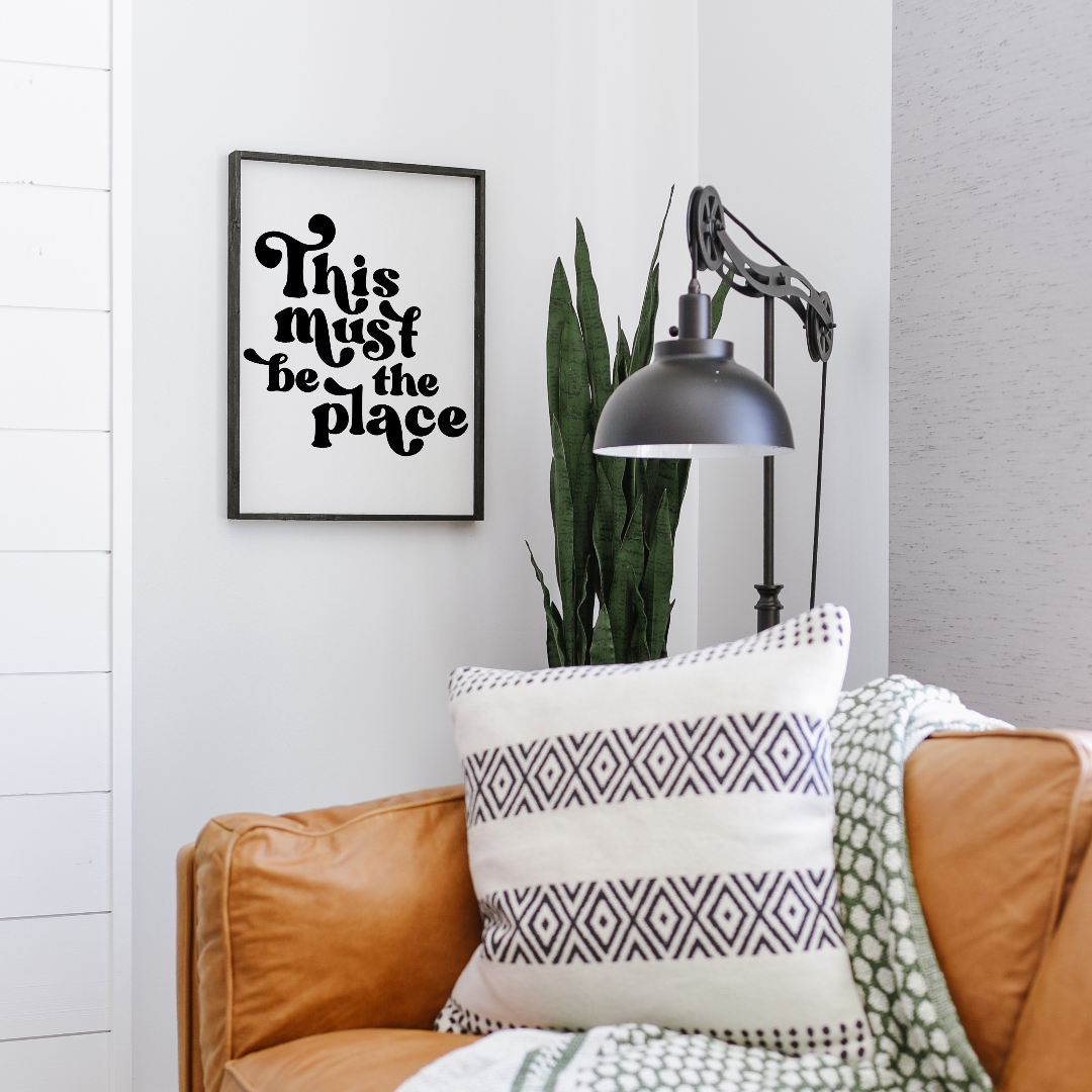 Living room with brown sofa, patterned pillow, and framed quote on wall.