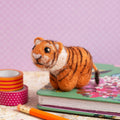 Plush tiger toy on a surface with notebooks and pencils against a purple background