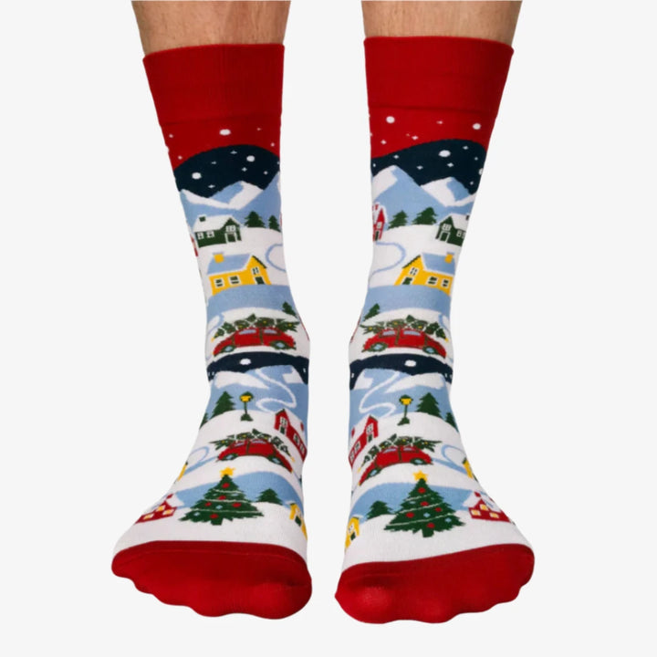 A pair of colorful socks with a winter scene. The socks feature houses, trees, and snowmen on a snowy landscape.