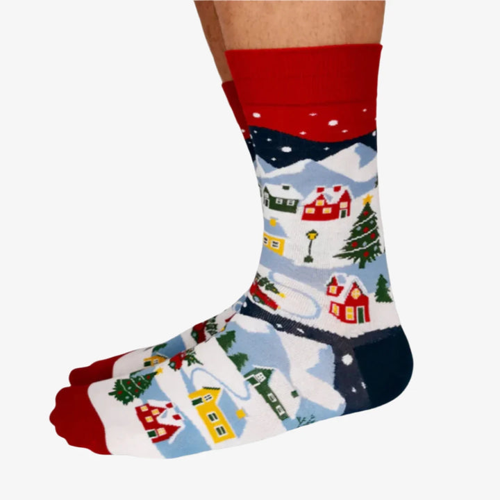A pair of colorful socks with a winter scene. The socks feature houses, trees, and snowmen on a snowy landscape.