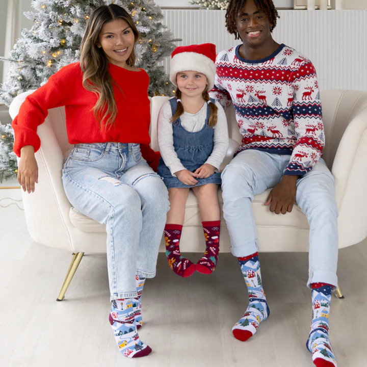 A pair of colorful socks with a winter scene. The socks feature houses, trees, and snowmen on a snowy landscape.