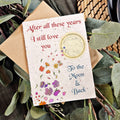 Greeting card with floral design and text 'After all these years I still love you To the Moon & Back' on a leafy background.
