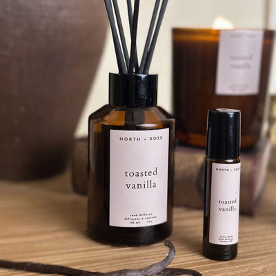 Diffuser and rollerball bottle labeled 'toasted vanilla' on a wooden surface.