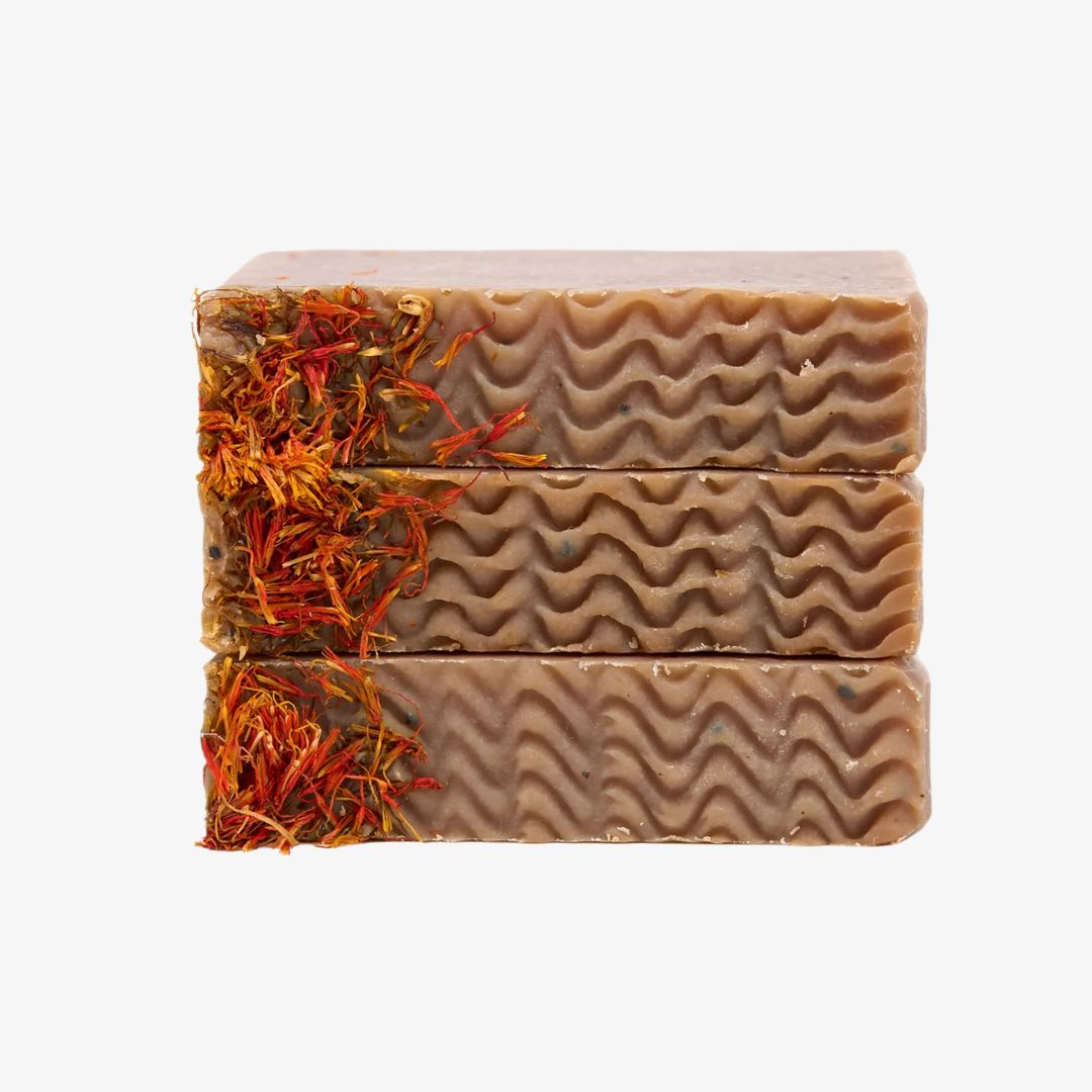 Three bars of soap with wavy texture and visible natural elements on a white background