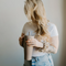 A cream-colored fabric scrunchie with a gathered, ruffled appearance. It features a delicate floral pattern in shades of brown, resembling dried flowers.