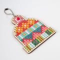 A wooden cross-stitch keychain shaped like a winter hat, featuring colorful embroidered patterns in red, orange, yellow, blue, pink, green, and white on a light wood base, complete with a silver metal key ring, set against a plain white background.
