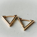 Gold triangle-shaped earrings on a light gray surface