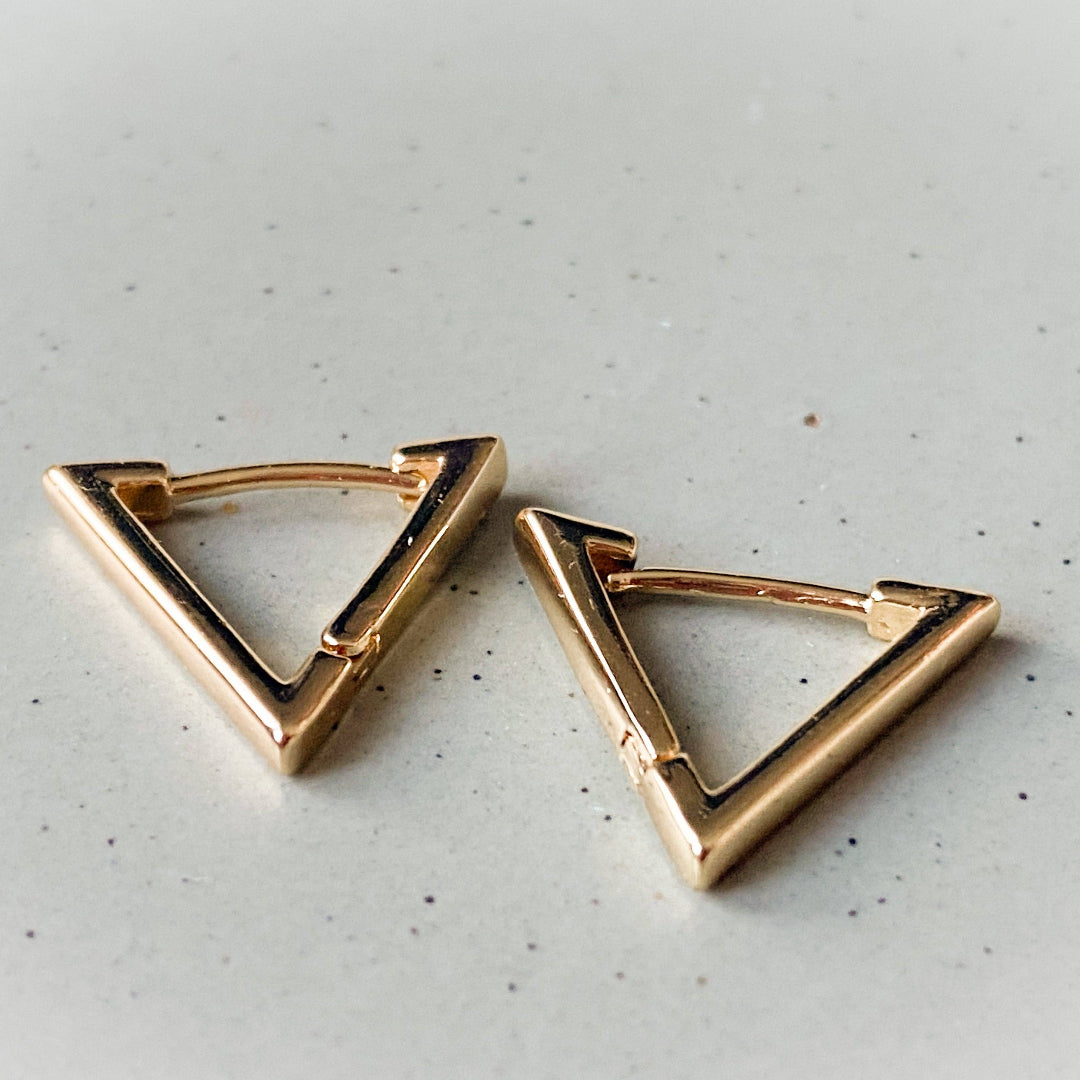 Gold triangle-shaped earrings on a light gray surface