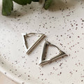 Triangular silver earrings on a speckled ceramic plate