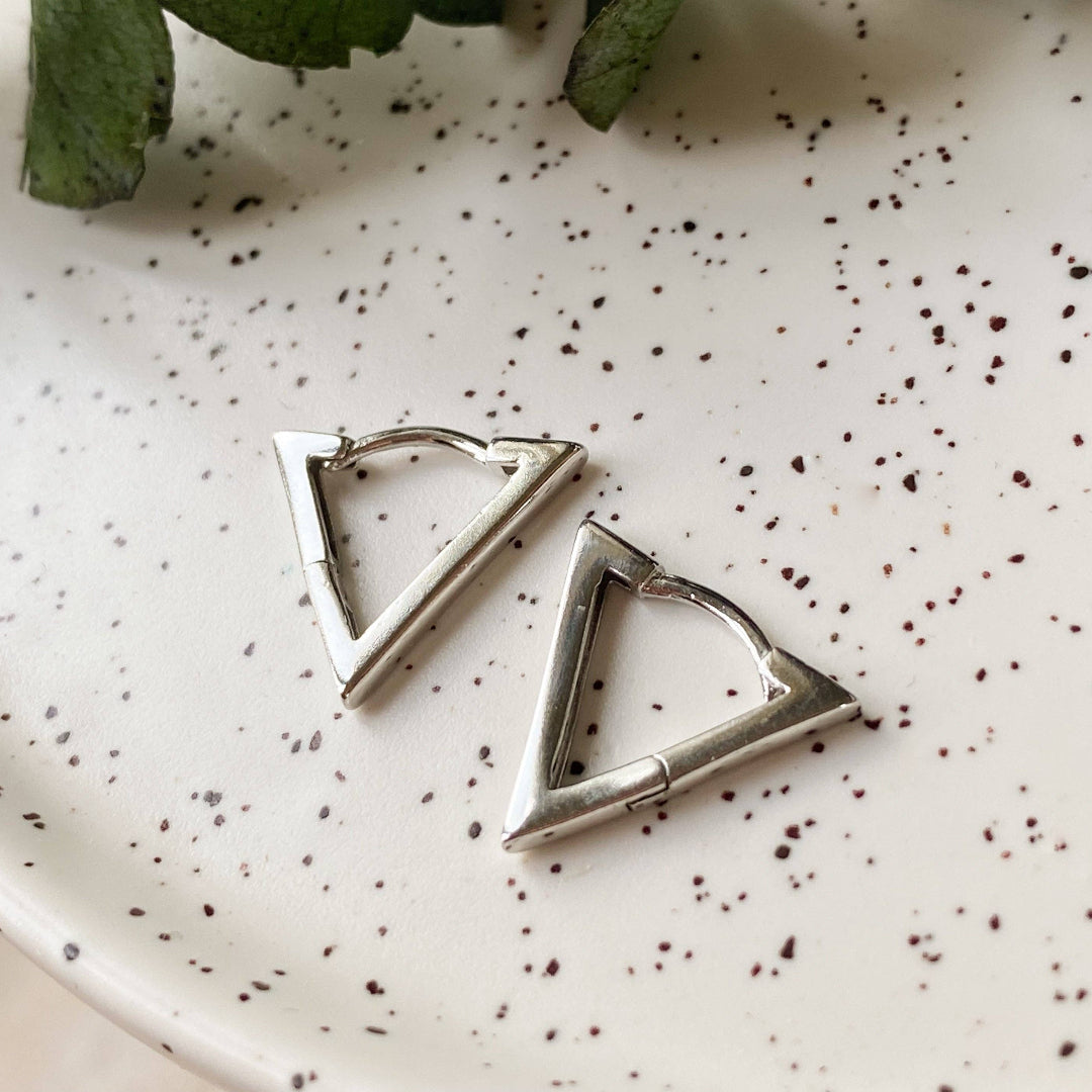 Triangular silver earrings on a speckled ceramic plate