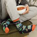 Person wearing colorful socks with cartoon designs, sitting on a chair holding a bowl of soup.