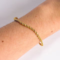 Gold rope chain bracelet on a wrist against a neutral background