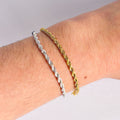 Two braided chain bracelets, one silver and one gold, on a wrist against a neutral background.