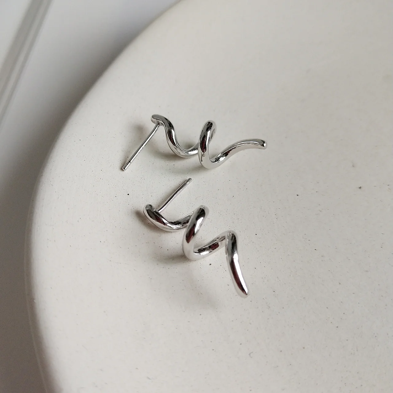 A pair of twisty coil earrings made of sterling silver, featuring a unique, abstract, and wavy design, displayed on a light-colored surface. These modern earrings are available in Ottawa, Ontario, Canada.