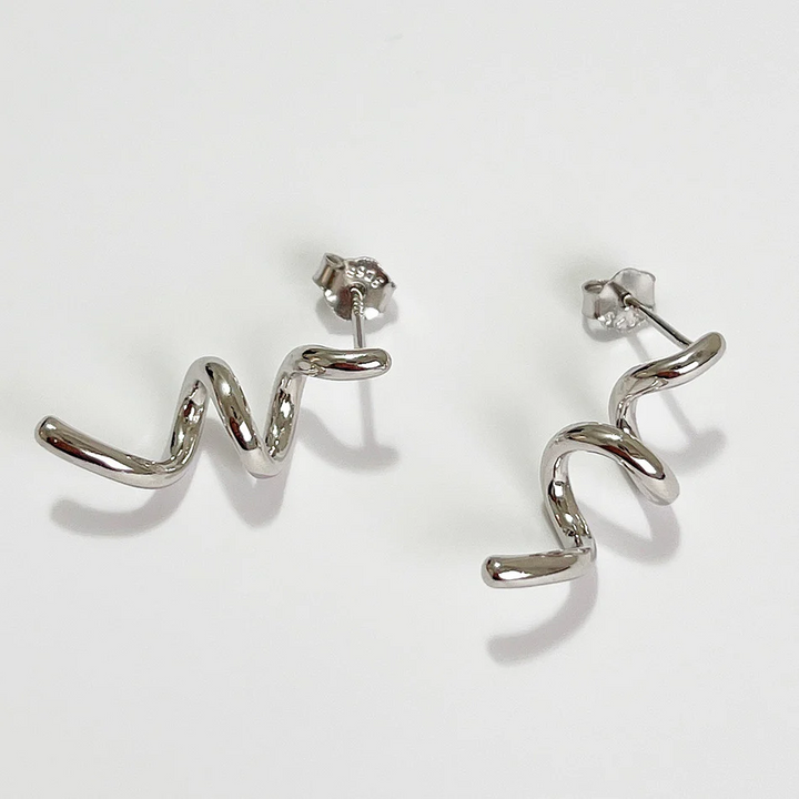 A pair of twisty coil earrings made of sterling silver, featuring a unique, abstract, and wavy design, displayed on a light-colored surface. These modern earrings are available in Ottawa, Ontario, Canada.