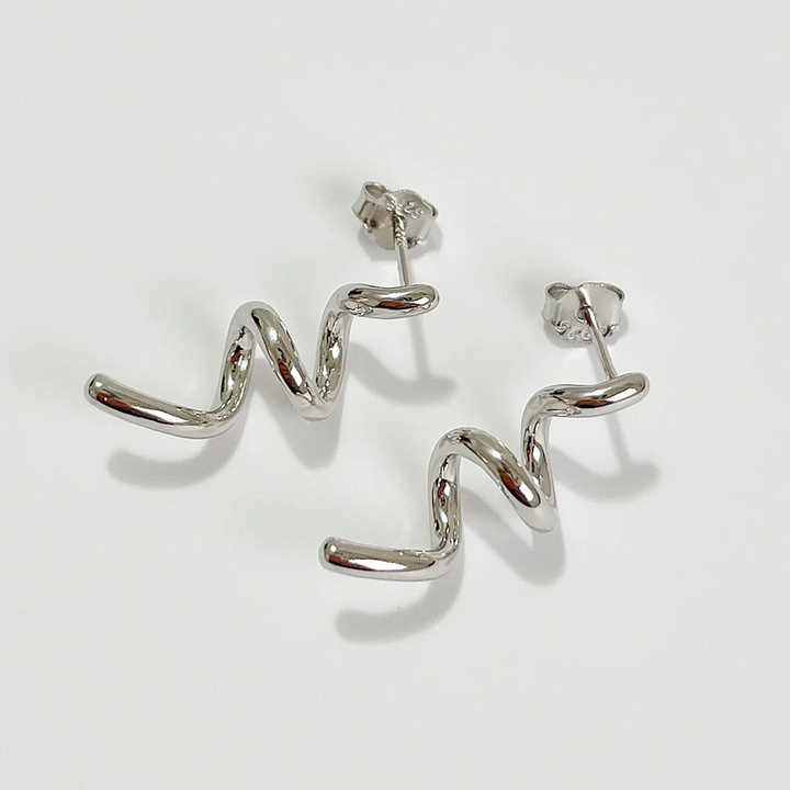 A pair of twisty coil earrings made of sterling silver, featuring a unique, abstract, and wavy design, displayed on a light-colored surface. These modern earrings are available in Ottawa, Ontario, Canada.