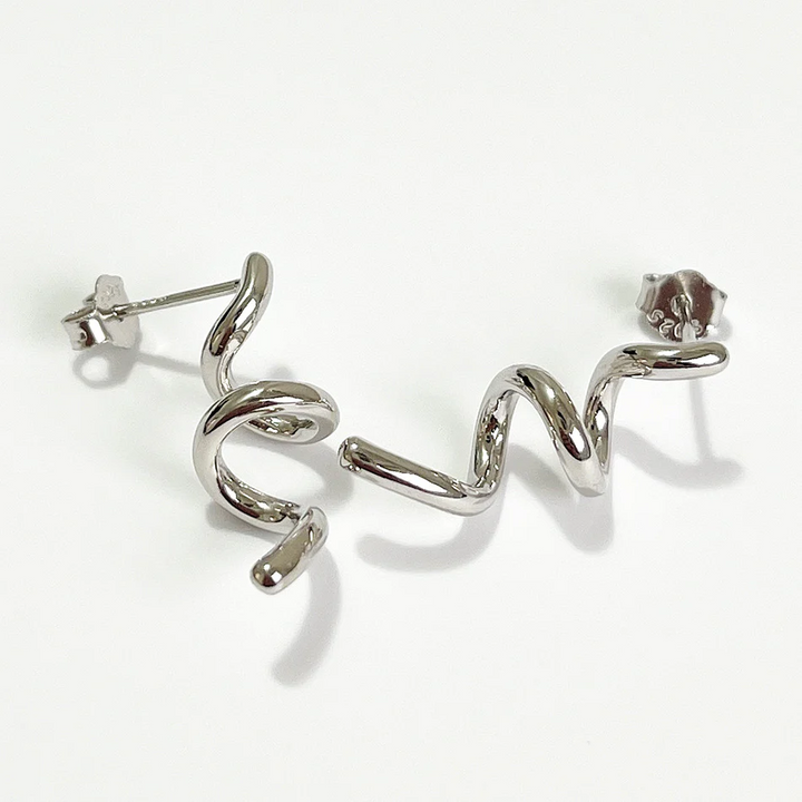 A pair of twisty coil earrings made of sterling silver, featuring a unique, abstract, and wavy design, displayed on a light-colored surface. These modern earrings are available in Ottawa, Ontario, Canada.