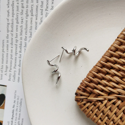 A pair of twisty coil earrings made of sterling silver, featuring a unique, abstract, and wavy design, displayed on a light-colored surface. These modern earrings are available in Ottawa, Ontario, Canada.
