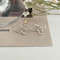 A pair of twisty knot stud earrings made of sterling silver, featuring a unique, abstract, and intertwined design, displayed on a book with dried flowers and a glass object. These modern earrings are available in Ottawa, Ontario, Canada.